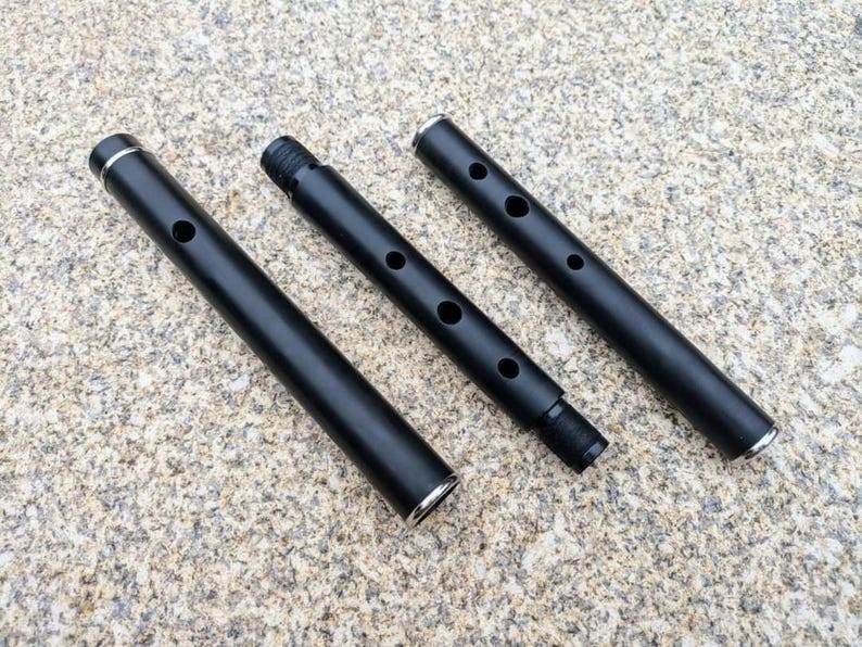 May include: Three black metal pipes with silver accents. The pipes are different lengths and have holes along the side.