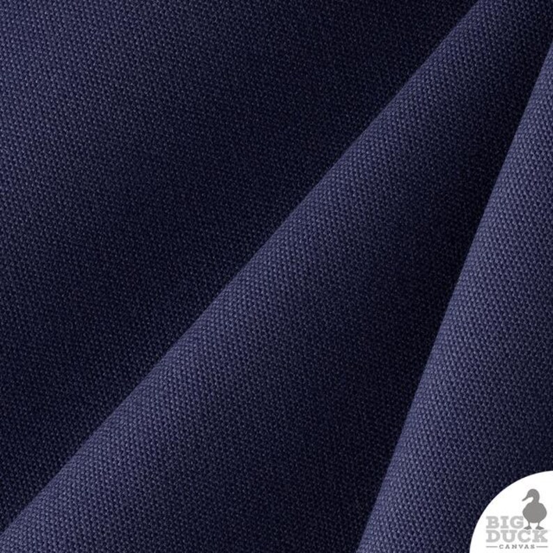 Pu&ograve; includere: Un tessuto in tela blu navy profondo con una trama fitta e distinta. Il materiale &egrave; piegato per creare ombre e riflessi diagonali sulla superficie. Nell'angolo in basso a destra, un logo bianco riporta la scritta BIG DUCK CANVAS.