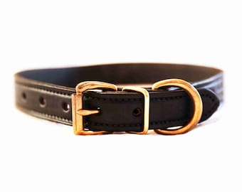 May include: A black leather dog collar with a gold-colored buckle and hardware. The collar has a classic design with a simple, elegant aesthetic. The collar is likely designed for a medium to large-sized dog.