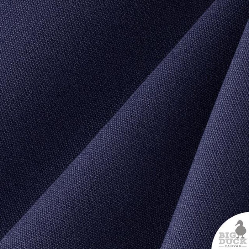 Op de afbeelding: Een diep marineblauwe canvasstof met een zichtbare geweven textuur en diagonale plooien. In de rechterbenedenhoek staat een wit cirkelvormig logo met een silhouet van een eend en de tekst BIG DUCK CANVAS in een strak, schreefloos lettertype.