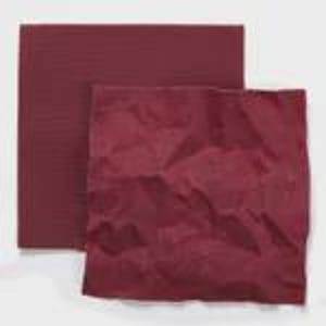 Op de afbeelding: Twee vierkante vellen donkerbordeauxrood papier. Het ene vel ligt achter het andere en ziet er glad en plat uit. Het voorste vel is verfrommeld, waardoor een getextureerd oppervlak met diverse vouwen en kreukels over het hele vierkante vlak ontstaat.
