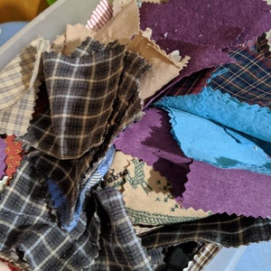May include: A clear plastic container filled with a variety of fabric scraps in different colors and patterns, including plaid, solid, and floral.