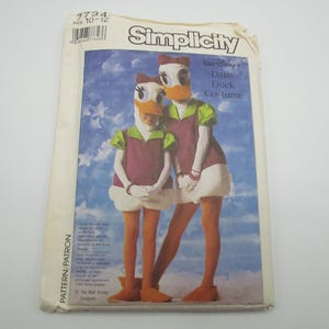 May include: A Simplicity sewing pattern envelope for a Walt Disney Daisy Duck costume, size 10-12. The cover features an illustration of two figures wearing purple and white dresses with green sleeves, white gloves, orange tights, and duck masks.