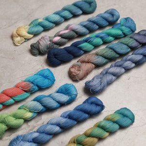 Peut inclure: Plusieurs écheveaux de fil coloré sont disposés en diagonale. Le fil présente une variété de teintes, notamment des bleus, des verts, des roses et des jaunes. Le fil semble doux et texturé, idéal pour les projets de tricot ou de crochet.