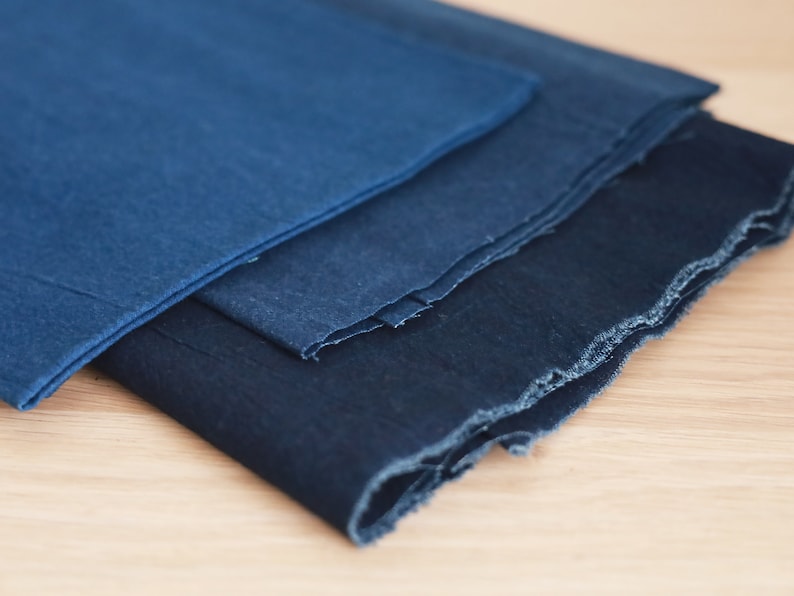 May include: Three pieces of indigo dyed fabric stacked on top of each other. The fabric is a deep blue color and has a rough, textured surface.