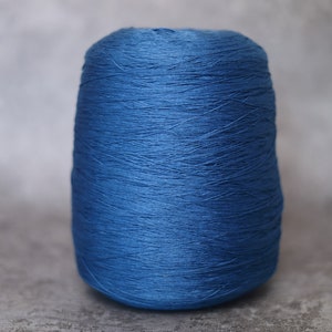 May include: A spool of vibrant blue yarn, tightly wound and cylindrical in shape. The yarn has a slightly textured appearance, suggesting a natural fiber. The background is a neutral gray, highlighting the yarn's color.