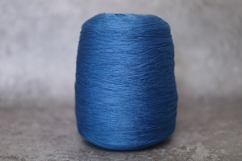 May include: A spool of vibrant blue yarn, tightly wound and cylindrical in shape. The yarn has a slightly textured appearance, suggesting a natural fiber. The background is a neutral gray, highlighting the yarn's color.