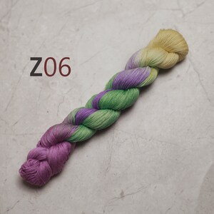 May include: A skein of yarn in shades of green, purple, and yellow. The yarn is twisted and has a gradient effect. The yarn is labelled "Z06". visible creative mending sashiko embroidery thread also quilting thread