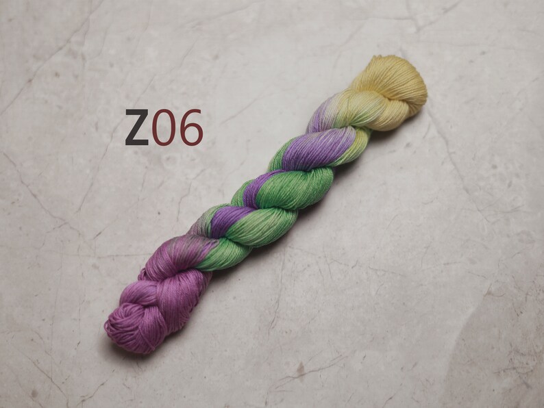 May include: A skein of yarn in shades of green, purple, and yellow. The yarn is twisted and has a gradient effect. The yarn is labelled "Z06". visible creative mending sashiko embroidery thread also quilting thread