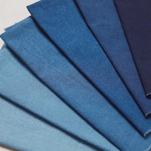 May include: A collection of eight fabric swatches in various shades of blue, ranging from light to dark. The swatches are arranged in a fan shape, with the darkest blue at the top and the lightest blue at the bottom.