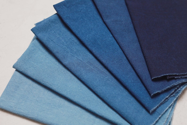May include: A collection of eight fabric swatches in various shades of blue, ranging from light to dark. The swatches are arranged in a fan shape, with the darkest blue at the top and the lightest blue at the bottom.