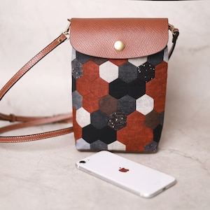 May include: A brown leather crossbody bag with a flap closure and a geometric patterned fabric lining. The bag has a long adjustable strap and a gold-toned buckle.