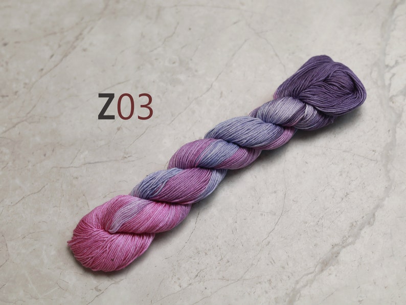 May include: A skein of yarn in shades of pink and purple. The yarn is twisted and has a gradient colour effect. The yarn is labelled "Z03".
