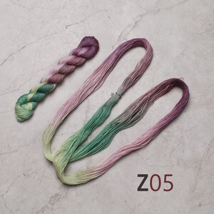 May include: Two skeins of embroidery floss, one green and yellow ombre and one pink ombre, with the text "Z05" on a grey background. visible creative mending sashiko thread