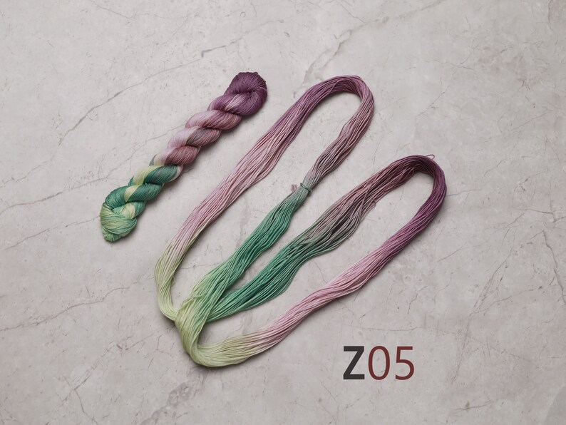 May include: Two skeins of embroidery floss, one green and yellow ombre and one pink ombre, with the text "Z05" on a grey background. visible creative mending sashiko thread