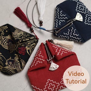 May include: Three Japanese-style fabric pouches in black, navy, and red. The black pouch features a gold fish design, the navy has a white geometric pattern, and the red has a white geometric pattern. Each pouch has a metal clasp and tassel.