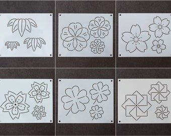 May include: Six white plastic stencils with different designs. The stencils feature various floral and geometric patterns, including leaves, flowers, and stars. The stencils are perfect for crafting and decorating projects.