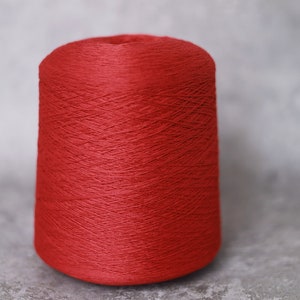 May include: A spool of vibrant red yarn, tightly wound and cone-shaped. The yarn has a smooth texture and is suitable for various knitting and crochet projects. The background is a neutral gray.