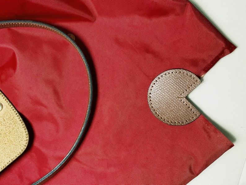 Puede incluir: Una bolsa de lona roja de nylon con un acento de cuero marr&oacute;n y una correa de cuero marr&oacute;n.