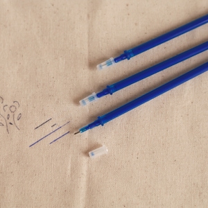 May include: Three blue ink pens with clear plastic caps on a beige fabric surface.