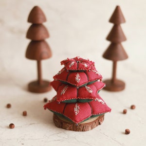 May include: A festive Christmas tree made of red and green fabric with silver accents. The tree is stacked on a wooden base and surrounded by small wooden beads.