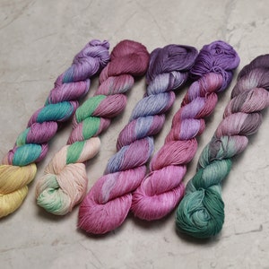 May include: Five skeins of hand-dyed yarn in various shades of pink, purple, green, and yellow. The yarn is twisted and has a subtle ombre effect. visible creative mending quilting thread