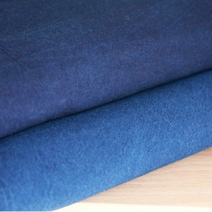 May include: Two pieces of indigo blue fabric folded on top of each other. The fabric has a textured surface and a slightly darker shade of blue on the top piece.