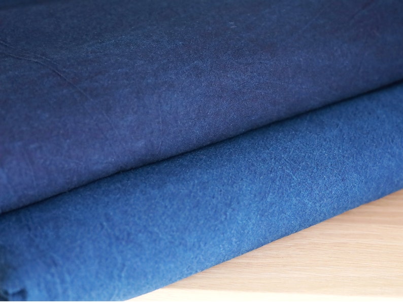 May include: Two pieces of indigo blue fabric folded on top of each other. The fabric has a textured surface and a slightly darker shade of blue on the top piece.