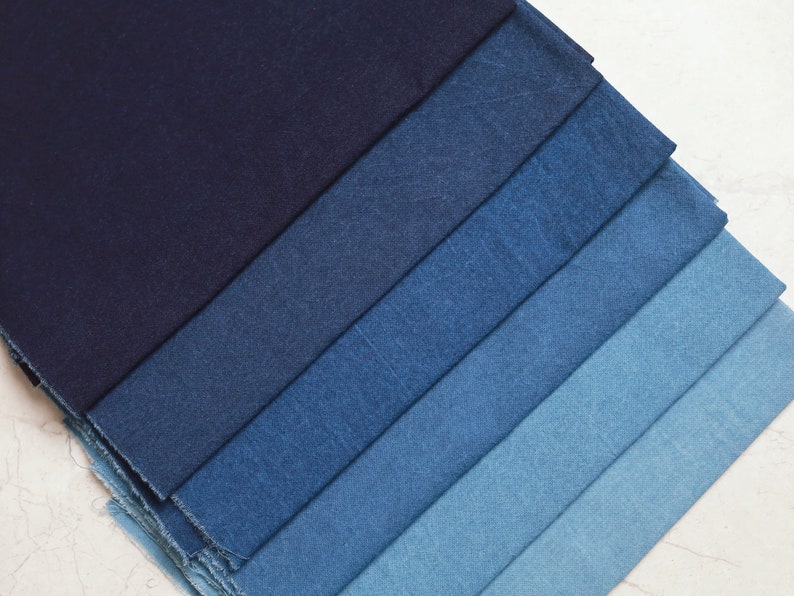 May include: A stack of denim fabric swatches in various shades of blue, ranging from dark indigo to light blue.