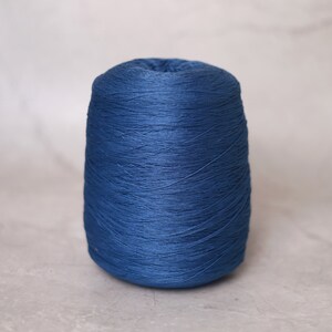 May include: A cone of dark blue yarn, tightly wound and textured. The yarn is a solid, saturated color, suitable for knitting or crocheting projects. The cone is centered against a neutral background.