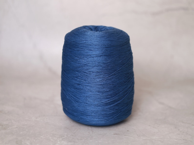 May include: A cone of dark blue yarn, tightly wound and textured. The yarn is a solid, saturated color, suitable for knitting or crocheting projects. The cone is centered against a neutral background.