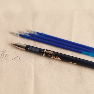May include: A blue and gold pen with a decorative design on the barrel. Four blue ink refills are also pictured.