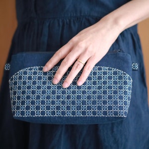 以下が含まれることがあります： 白い幾何学模様が刺繍された濃い青色の布製のポーチ。ポーチは上部が丸く、ジッパーで閉じられます。