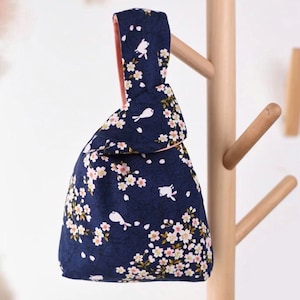 Pu&ograve; includere: Una borsa tote in tessuto blu navy con un motivo floreale rosa e bianco e piccoli uccelli bianchi. La borsa ha un manico annodato.