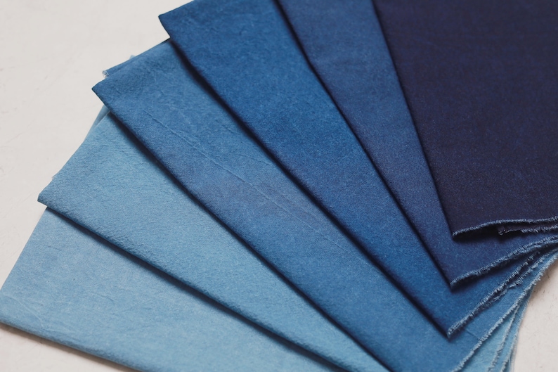 May include: A collection of eight fabric swatches in various shades of blue, ranging from light to dark. The swatches are arranged in a fan shape, with the darkest blue at the top and the lightest blue at the bottom.