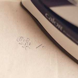 May include: A white iron with the word "Calor" printed on it is being used to press a small floral design onto a piece of white fabric.