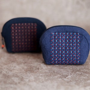 Peut inclure: Deux trousses de toilette en tissu bleu avec un motif tissé rouge et blanc. Les trousses sont sur une surface texturée brune.