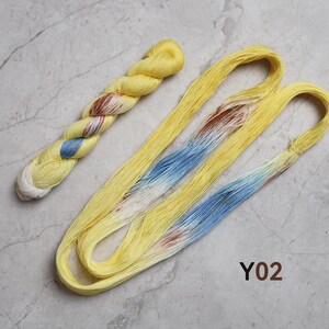 May include: Two skeins of yarn, one twisted and one loose, featuring a primary bright yellow color with variegated sections of light blue, white, and reddish-brown. The text Y02 is printed in brown near the bottom right of the yarn arrangement.