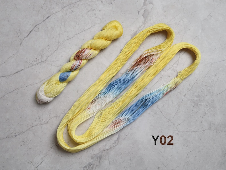 May include: Two skeins of yarn, one twisted and one loose, featuring a primary bright yellow color with variegated sections of light blue, white, and reddish-brown. The text Y02 is printed in brown near the bottom right of the yarn arrangement.