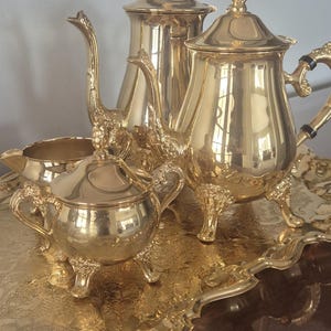 May include: A gold-plated tea set with a teapot, creamer, sugar bowl, and tray. The set features ornate details and a classic design.