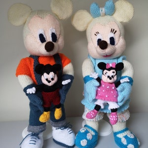 以下が含まれることがあります： 編みぐるみで作られたミッキーマウスとミニーマウスの人形。ミッキーはオレンジ色のセーター、青色のオーバーオール、黄色の靴、白いスニーカーを着用しています。ミニーは青いドレス、リボンを身につけ、小さなミニーの人形を持っています。どちらの人形も大きな耳と笑顔の顔をしています。