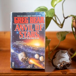 May include: A paperback book titled "Anvil of Stars" by Greg Bear, the sequel to "The Forge of God". The cover features a colorful illustration of a spaceship in space.