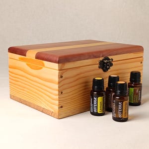 May include: A wooden box with a hinged lid and a brass latch. The box is made of light wood with a darker wood inlay. There are five small glass bottles with labels that say "dōTERRA" and the names of essential oils: Lemon, Eucalyptus, Wild Orange, and Tea Tree.