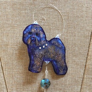 May include: A blue and brown patterned glass ornament of a Bichon Frise dog with a crystal dangle.