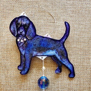 May include: A blue and purple painted wooden ornament of a beagle dog with a crystal bead hanging from it.
