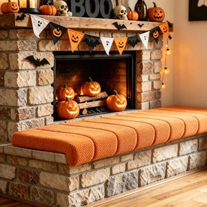 May include: A stone fireplace hearth featuring a textured orange bench cushion. The mantel is decorated with a Halloween bunting of ghosts, bats, and jack-o'-lanterns, along with skulls, pumpkins, and a black sign reading BOO.