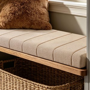 May include: A wooden storage bench featuring a beige upholstered seat with vertical channel tufting. A brown faux fur pillow rests on the seat, and a woven wicker basket is positioned underneath the bench on the lower shelf for storage.