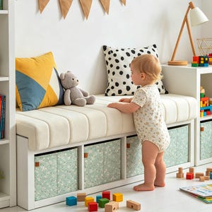 May include: A white storage bench with a tufted cushion top, featuring three lower cubbies containing light green floral fabric bins. The bench is decorated with a yellow and blue geometric cushion, a polka dot cushion, and a grey teddy bear.