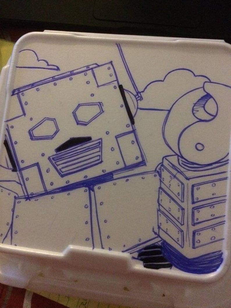 Puede incluir: Un dibujo a l&iacute;nea azul y negro de un robot en un contenedor de poliestireno blanco. El robot tiene una cabeza grande con un cuerpo cuadrado y un brazo peque&ntilde;o.