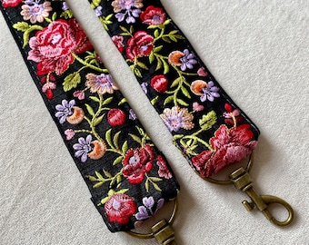 May include: Two black straps with floral embroidery in shades of pink, red, green, and purple. Each strap has a gold metal clasp.